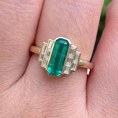 a close up of a person's hand wearing a ring with an emerald and diamond