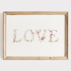 the word love is made up of flowers and leaves on a white background, framed in an antique wood frame