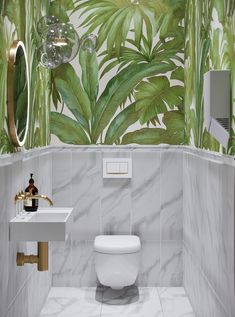 a white toilet sitting next to a sink in a bathroom under a green leaf wallpaper