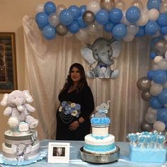 a woman standing in front of a table with blue and white cakes, balloons and decorations