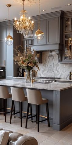 an elegant kitchen with gray cabinets and marble counter tops, chandelier above the island