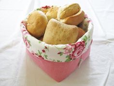 a basket filled with rolls sitting on top of a white table covered in pink and green flowers