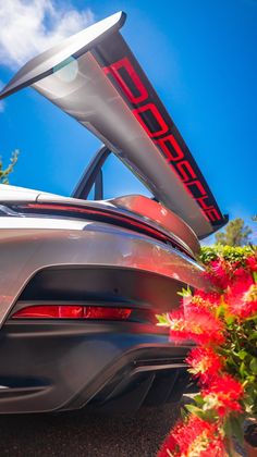 the back end of a sports car with its trunk open and flowers growing in front