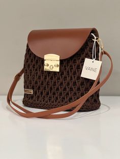 a brown handbag with a name tag on the front and shoulder strap, sitting on a white surface