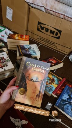 a person is holding up a book in front of several boxes on the floor with other books