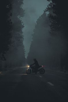 a man riding on the back of a motorcycle down a dark road