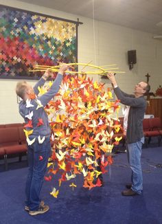 two men standing next to each other holding up origami cranes