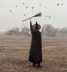 a man in a black cloak and hat holding a broom with birds flying above him