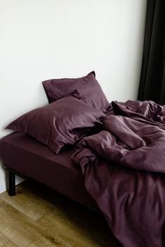 an unmade bed with purple sheets and pillows