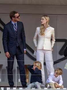 two men and one woman are standing on the sidelines with their children in front of them