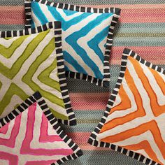 four different colored pillows sitting on top of a colorful bed sheet with black and white stripes