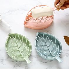 three leaf shaped dishes are shown on a marble countertop, one is being dipped with soap and the other is holding a toothbrush