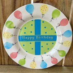 a happy birthday plate with balloons on it sitting on a shelf next to a wooden wall