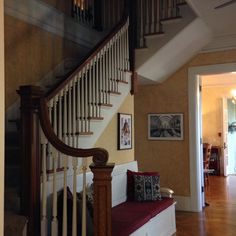 the stairs in this house are made of wood and have white railings with red cushions on them