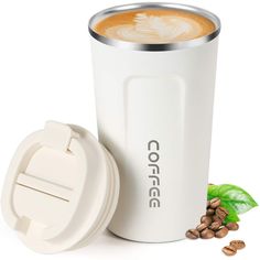 a white coffee cup sitting next to a container filled with coffee beans and green leaves