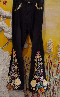 a pair of black jeans with flowers on them hanging up against a yellow and white wall