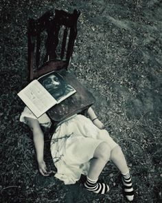 a woman laying on the ground next to a chair with an open book in her lap