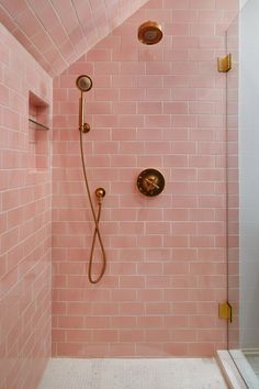 a pink tiled shower in a bathroom with gold fixtures on the faucet and hand held shower head