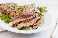 a white plate topped with sliced meat and garnished with parsley next to a fork