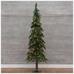 a small christmas tree with lights on it's branches in front of a wooden wall