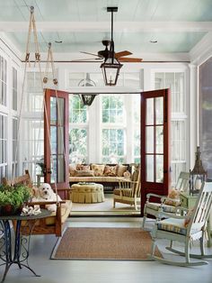 a living room filled with lots of furniture next to two large windows and a ceiling fan