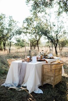 a table set up for an outdoor dinner in the woods with candles and food on it