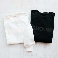 two black and white sweaters sitting next to each other on a wooden surface with the word groom printed on them