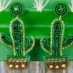 green and gold cactus earrings with beads on it's backs, against a green background