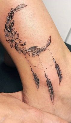 a woman's foot with a tattoo on it that has flowers and feathers flying around