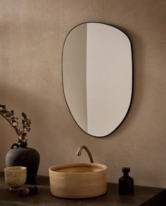 a bathroom sink with a round mirror on the wall above it and a vase next to it