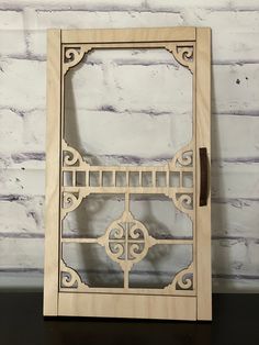 a wooden frame with an intricate design on it, sitting against a white brick wall