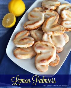 lemon palmiers on a white plate next to sliced lemons and a blue table cloth