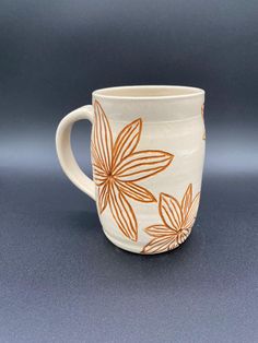 a white coffee cup with orange flowers on the outside and inside, sitting on a gray surface