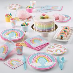 a table topped with lots of colorful plates and desserts next to a cake covered in rainbow icing