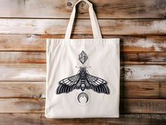 a white tote bag with a black and white moth design on it hanging from a wooden wall