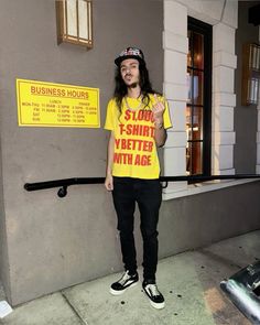 a man in a yellow shirt and black pants stands on the sidewalk with his hand up