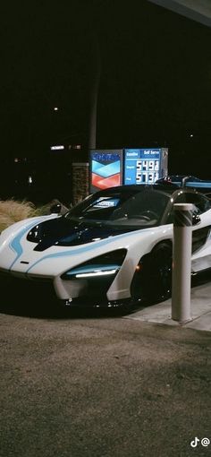 a white and blue sports car parked in front of a parking meter at night time