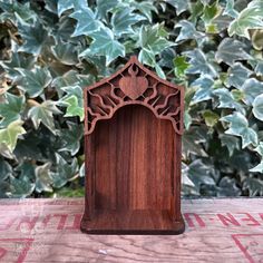 a wooden block with an intricate design on the front and sides, sitting in front of some green leaves