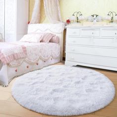 a bedroom with a white bed, dresser and rug on the floor in front of it