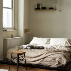 an unmade bed with white sheets and pillows in a bedroom next to a window