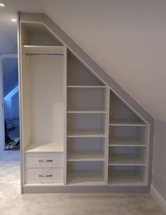 an attic bedroom with built in shelving and closet space under the roof, white walls and carpeted flooring