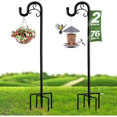 two bird feeders are hanging from black metal stands on green grass with flowers in the background