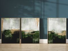 three abstract paintings are displayed in front of a blue wall and hardwood flooring area