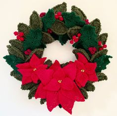 a knitted christmas wreath with poinsettis and holly leaves on white background