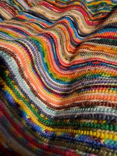 a multicolored crocheted blanket is laying on top of a tablecloth