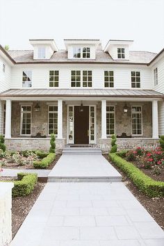 a large white house with lots of windows and plants on the front lawn, along with steps leading up to it