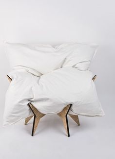 a bed with white sheets and pillows on it's legs in front of a white wall