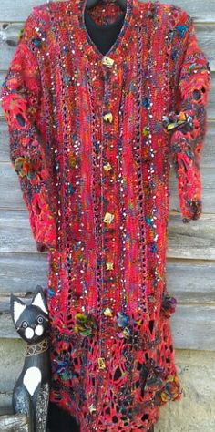 a woman's red sweater hanging up against a wooden wall with beads on it