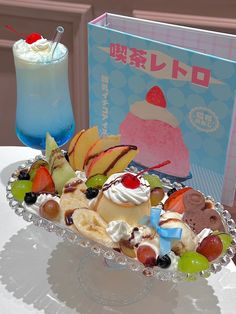 a plate with fruit and ice cream on it next to a blue drink in front of a book