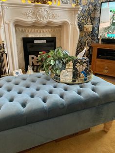 a living room with a blue ottoman and television in the fireplace mantel, along with a potted plant on top